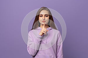 Portrait of beautiful young european woman with chestnut hair holding index finger at lips, asking to keep silence or not tell