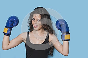 Portrait of a beautiful young female boxer raising arms in victory against blue background