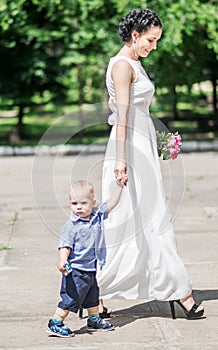 Portrait of a beautiful young female bride walking with small baby boy to wedding ceremony. Mother and her little son on her weddi