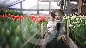 Portrait of beautiful young female smiling woman worker florist in apron and hat typing on tablet browsing online in