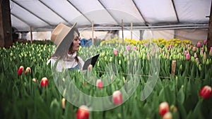 Portrait of beautiful young female smiling woman worker florist in apron and hat typing on tablet browsing online in