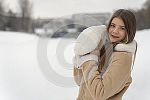 Portrait of a beautiful young girl in a beige coat on a background of winter landscape. Copy space