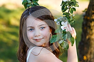 Portrait of a beautiful young girl with blue eyes in white dress in the garden with apple trees blosoming at the sunset