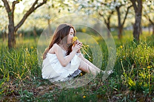 Portrait of a beautiful young girl with blue eyes in white dress in the garden with apple trees blosoming at the sunset