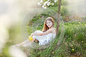 Portrait of a beautiful young girl with blue eyes in white dress in the garden with apple trees blosoming at the sunset