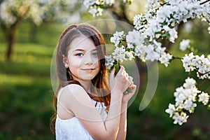 Portrait of a beautiful young girl with blue eyes in white dress in the garden with apple trees blosoming at the sunset