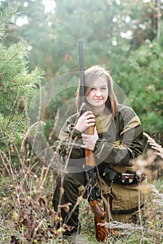 Portrait of a beautiful young girl in camouflage hunter with shotgun