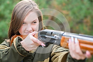 Portrait of a beautiful young girl in camouflage hunter with shotgun