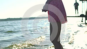 Portrait of a beautiful young girl doing splashes with her foot standing in the water on a background of beach and sky