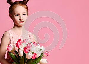 Portrait of a beautiful young girl in dress holding big bouquet of irises and tulips isolated over pink background