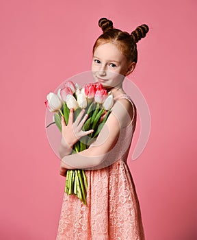 Portrait of a beautiful young girl in dress holding big bouquet of irises and tulips isolated over pink background