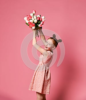 Portrait of a beautiful young girl in dress holding big bouquet of irises and tulips isolated over pink background