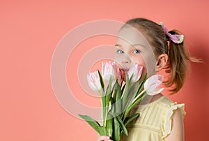 Portrait of a beautiful young girl in dress holding big bouquet of tulips isolated over pink background