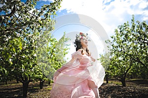 Portrait of a beautiful young girl in a flying bride tender pink dress on a background of green field, she laughs and poses with a