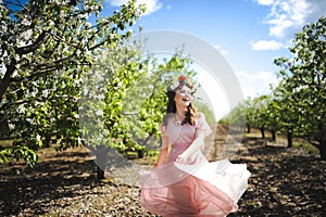 Portrait of a beautiful young girl in a flying bride tender pink dress on a background of green field, she laughs and poses with a