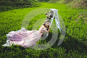 Portrait of a beautiful young girl in a flying bride tender pink dress on a background of green field, she laughs and poses with a