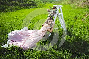 Portrait of a beautiful young girl in a flying bride tender pink dress on a background of green field, she laughs and poses with a