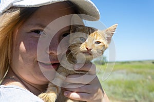 Portrait of a beautiful young girl. The girl holds a ginger kitten in her arms. Walk in the summer with a pet outdoors