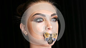 Portrait of a beautiful young girl model with fashionable smoky eyes makeup and a butterfly on her lips posing in front