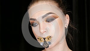 Portrait of a beautiful young girl model with fashionable smoky eyes makeup and a butterfly on her lips posing in front