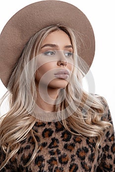 Portrait of a beautiful young girl with natural make-up with lips with long curly blond hair in an elegant hat