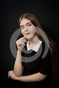 Portrait of a beautiful young girl with straight long hair and blue eyes, in black clothes on a black background, waist-deep, with