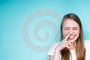 Portrait of a beautiful young girl touching her nose with her finger and closing her eyes laughing