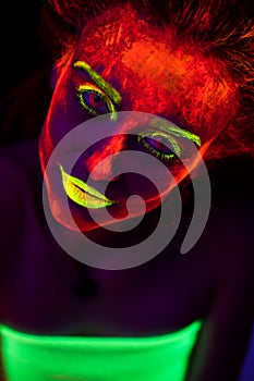 Portrait of a beautiful young girl with ultraviolet paint on her body and glowing contact lenses looking in camera