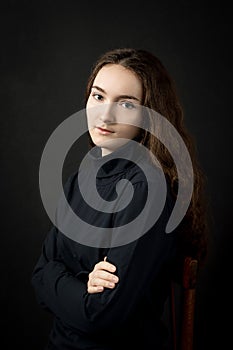 Portrait of a beautiful young   girl with wavy long hair and blue eyes, in black clothes on a black background, waist-deep, with a