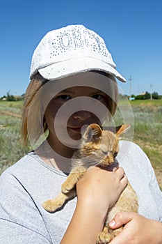 Portrait of a beautiful young girl in a white cap. Red kitten in the hands of his mistress. Walk with your pet in the summer