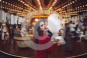 Portrait of a beautiful young girl with white cotton candy in front of a carousel horse