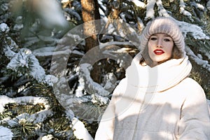 Portrait of beautiful young girl in winter in park against snowy pine trees background. Sunny winter day