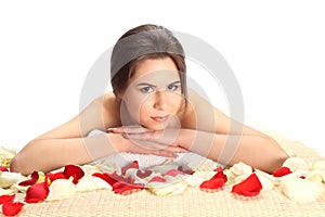 Portrait of Beautiful, young and healthy woman in spa salon on bamboo mat with rose petals. Spa, health and healing concept.