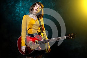 Portrait of beautiful young hipster woman with curly hair with red guitar in neon lights. Rock musician is playing