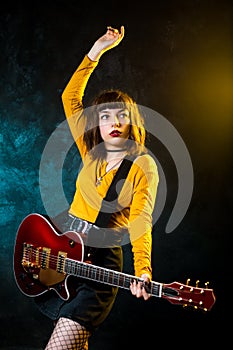 Portrait of beautiful young hipster woman with curly hair with red guitar in neon lights. Rock musician is playing