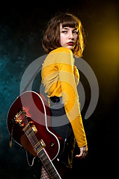 Portrait of beautiful young hipster woman with curly hair with red guitar in neon lights. Rock musician is playing