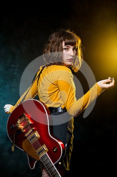 Portrait of beautiful young hipster woman with curly hair with red guitar in neon lights. Rock musician is playing