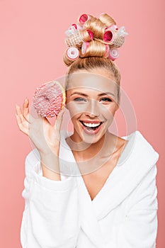 Portrait of beautiful young housewife in housecoat with hair curlers smiling while holding sweet donut photo