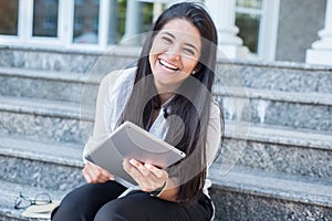 Portrait of a beautiful young Indian girl, business woman, smiling, sitting on the steps, looking into tablet