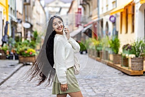 Portrait of a beautiful young Indian woman with long hair walking on a city street, talking on the phone, posing and