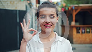 Portrait of beautiful young lady smiling showing OK hand gesture outdoors