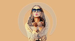 Portrait of beautiful young lady woman blowing her lips sends sweet air kiss wearing sunglasses on beige studio background