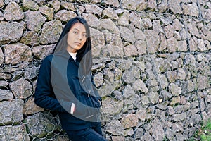 Portrait of a beautiful Young Latin woman with black hair and casual clothes leaning against a stone wall background with space