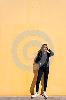 Portrait of a beautiful Young Latin woman with black hair and casual clothes leaning against a yellow background with space for