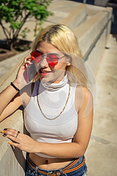 Portrait of a beautiful young Latina woman in a white t-shirt standing next to a railing while talking smiling on a cell phone