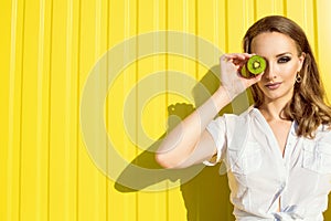 Portrait of beautiful young model with long hair and provocative artistic make-up hiding her eye behind the split kiwi fruit