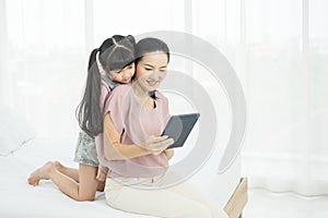 Portrait of beautiful young mom with girl sitting on the bed in a moment of intimacy while buying products online with tablet,.