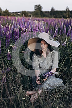 Portrait of a beautiful young mom in a hat with a lupine flower in her hands.