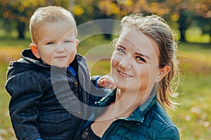 Portrait of a beautiful young mother with her son walks in the autumn park