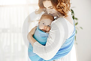 Portrait of beautiful young mother holding tight her newborn baby boy with love and caring. She smiling and feeling